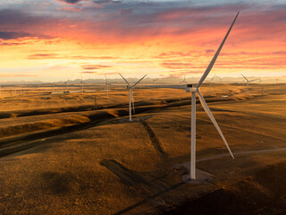Aerial sunset windmills producing sustainable energy over natural grasslands with mountains at background near Pincher Creek Alberta Canada under a colourful dramatic sky.