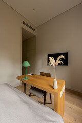 wooden desk and chair near tv flat screen on wall in hotel room.