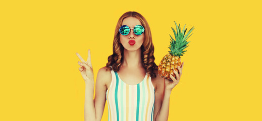 Summer portrait of young woman blowing her lips with pineapple wearing sunglasses posing on yellow...