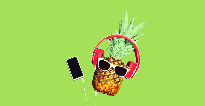 Colorful trendy image of stylish pineapple in wireless headphones listening to music with smartphone on green background