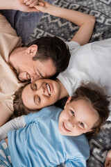 top view of joyful parents with closed eyes and happy kid lying on bed at home.