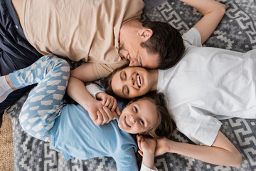 top view of pleased parents and cheerful kid lying on bed at home.