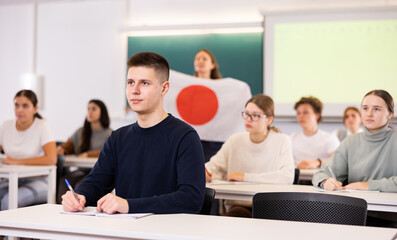 Fototapeta premium Students sit in classroom, teacher stands behind with flag of Japan