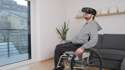 Man with disability on wheelchair using virtual reality equipment, VR headset to look around metaverse and the virtual world from his home, side view.