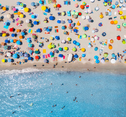 Aerial view of colorful umbrellas on sandy beach, people in blue sea at bright sunny day in summer....