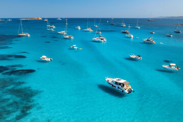 Aerial view of luxury yachts on blue sea at sunny day in summer. Sardinia, Italy. Aerial view of speed boats, yachts, sea lagoon, shore, transparent water, sky. Top view from drone. Tropical seascape	