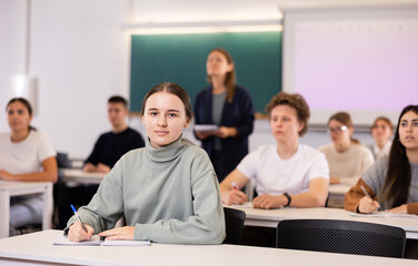 Fototapeta premium Female college student is sitting at desk and writing in book