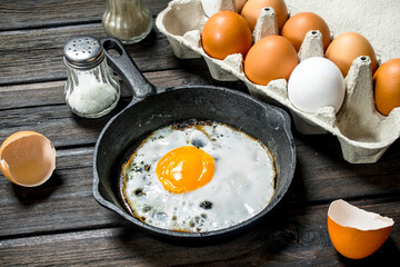 Fried egg in a pan with a cassette of fresh eggs.