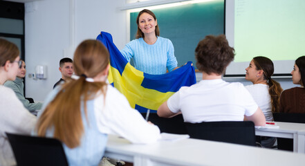 Fototapeta na wymiar Confident young female professor shows students flag of Sweden