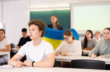 Students study in classroom, teacher stands behind with flag of Ukraine