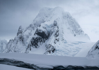 Mountain snowy peaks of Petermann Island in Antarctica, wit overcast grey sky. 