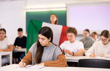 Fototapeta premium High school teacher tells students about Italy and holds a Italy flag in her hands.