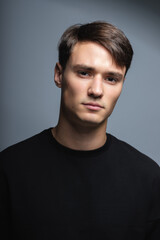 A guy of model appearance in black clothes poses on a gray studio background. Male fashion portrait