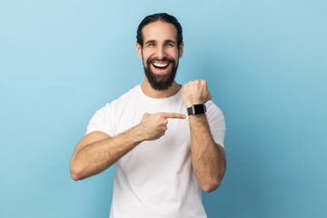 Look at clock, no rush. Portrait of man with beard wearing white T-shirt pointing wrist watch and...