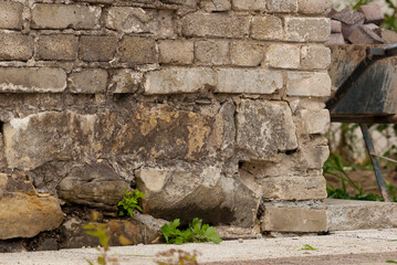 Fototapeta na wymiar Ceglana ściana starego zabytkowego budynku . Częściowo widoczny fundament z kamienia łupanego na bloczki . Z boku taczka z kostką brukową .