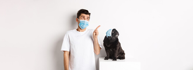 Covid-19, animals and quarantine concept. Young man and black dog wearing medical masks, pug and...