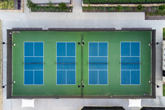 View from above, aerial view of four blue public, empty tennis courts, tennis playgrounds in the summertime outdoor.