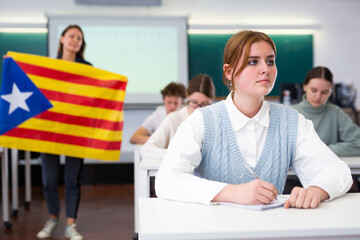 Geography lesson in school class - teacher talks about Catalonia, holding a flag in his hands - obrazy, fototapety, plakaty