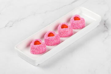 Vegan festive dessert. Small Strawberry cream mousse cake with jelly filling, in the shape of a heart, sprinkled with pink coconut chips. On a plate. White background. Valentine's day