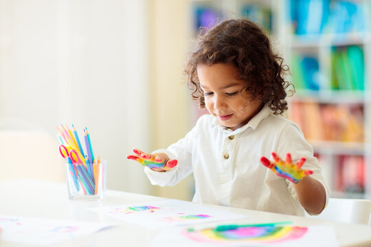 Child drawing rainbow. Paint on hands.