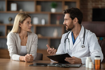 Smiling Doctor Man Talking ToFemale Patient During Appointment In Office