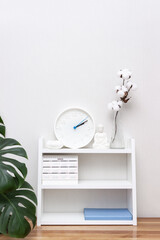 Buddha figurine, clock, candlestick, calendar and blue notebook surrounded by monstera and vases with branch of cotton on shelf. Mental health concept. Vertical banner, selective focus, copy space