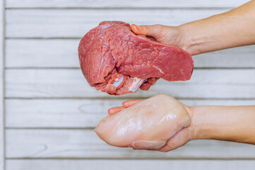 The girl holds in her hands large pieces of raw meat of beef and chicken on a wooden background....