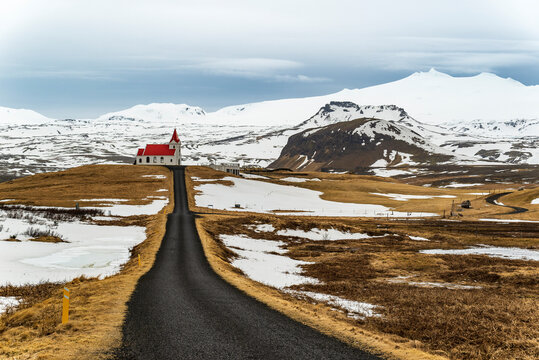Road leading towards the small church of Ingjaldsh&oacute;ll, the Ingjaldsh&oacute;lskirkja, with the snow-covered Sn&aelig;fellsj&ouml;kull glacier in the background, near Hellissandur, Sn&aelig;fellsnes, Iceland