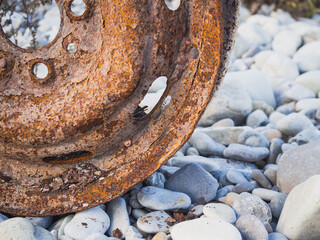 Old car wheel, rusty car alloy rim on stones by the river