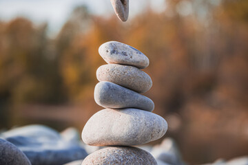 A young woman building a tower of stones with her hand on the riverside, along the shoreline. Yoga woman calm relaxation meditation harmony life balance equilibrium balance pyramid