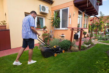 Young smiling man gardener mowing the lawn with lawnmower in summer	