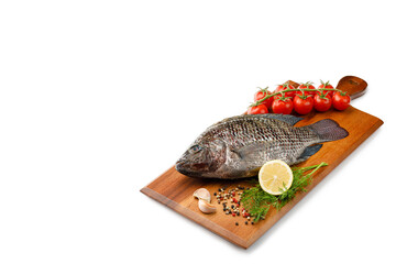 Raw fish Tilapia with spices and herbs ingredients for cooking, lemon and tomatoes on wooden...