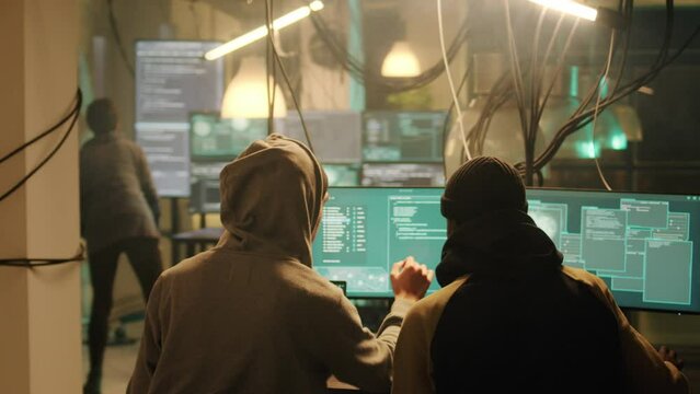 Anonymous men working together to break network system on computer, stealing info and passwords. People planting virus and doing phishing for ransomware, cyberbullying or harassment.