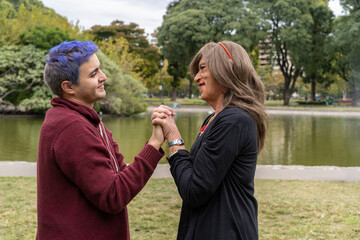 Transgender woman and her gay son holding hands and lovingly looking at each other in a park.