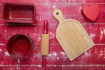 rolling pins, cookie cutters, and flour on a red wooden background. Heart and cutting board. View...