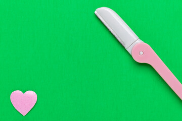 Pink disposable razor blade on green background. Single use razor blade. Disposable shaving razor. Body care.