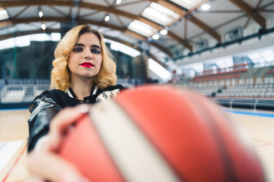 Blond cheerleader in a black jacket holding a ball in front of a camera. Blurred foreground. Sport concept. High quality photo