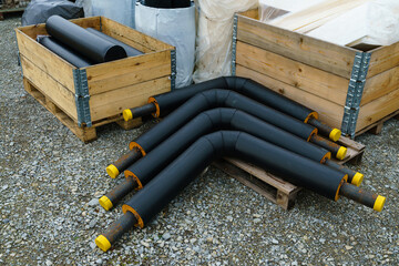 Angled insulated heating pipes with yellow plastic plugs lie on the construction site.. Next to...