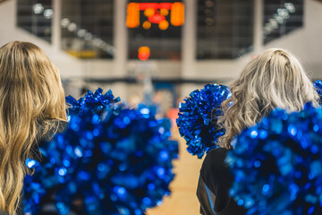 Back shot of the heads of two cheerleaders hodling blue pom-poms. Blurred background. High quality...
