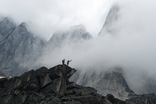 Two hikers on rocky spire in misty mountains, Bugaboo Provincial Park, Radium, British Columbia, Canada.