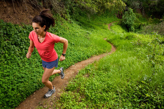 Woman trail running through a green meadow in the woods.