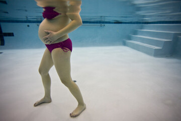 Pregnant woman in bikini in indoor swimming pool relaxing during later stages.