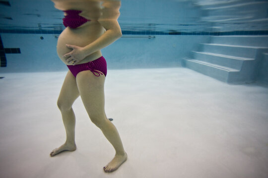 Pregnant woman in bikini in indoor swimming pool relaxing during later stages.