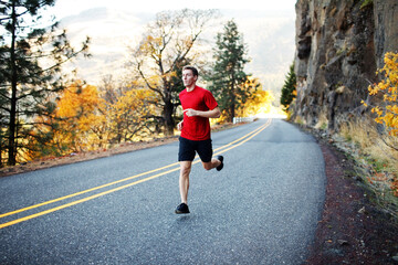 Male runner in his mid 20s running along scenic road in Rowena
