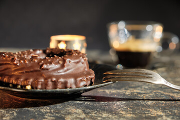 a chocolat nougat ring on a plate with a pastry fork, A glassy espresso cup and a candle light is in the bookeh