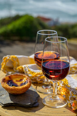 Portugal's traditional food and drink, glass of porto wine, muscatel de setubal and dessert Pastel de nata egg custard tart pastry served with view on blue Atlantic ocean in Lisbon area, Portugal