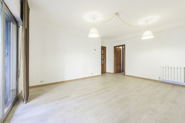 Empty room with light wooden flooring, white aluminum radiator, sapele wood access doors and twin lamps on the ceiling