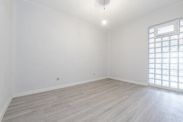 Empty room with skylight wall made of square glass pavers and light wooden floor