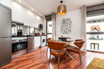 Loft-style vacation rental apartment with an open kitchen with windows to the street and a circular glass dining table and chairs upholstered in brown leather