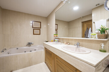 Bathroom with hydromassage bathtub with marble tiles, two sinks on the countertop with wooden furniture with Venetian-style doors under the frameless mirror